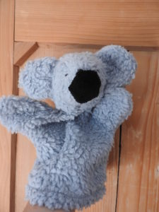 Koala Handpuppe aus grauem Kunstfell. Er hat die Arme offen ausgebreitet